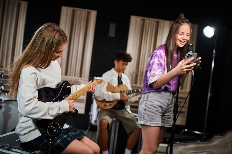 jolly cute teenage girl in everyday attire singing happily next to her friend on guitars in studio, stock photo. jolly cute teenage girl in everyday attire singing happily next to her friend on guitars in studio, stock photo