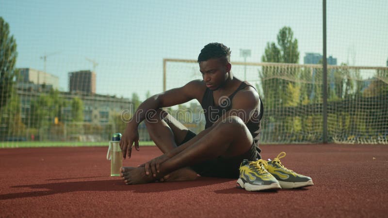 Jogador de futebol americano africano sentado no campo sofre dor dor forte dor muscular cãibras no pé ferido desportista ferido