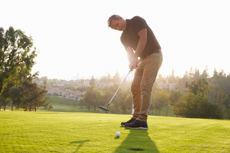 Jogador de golfe masculino que põe a bola no furo sobre o verde imagens de stock Jogador de golfe masculino que põe a bola no furo sobre o verde imagens de stock