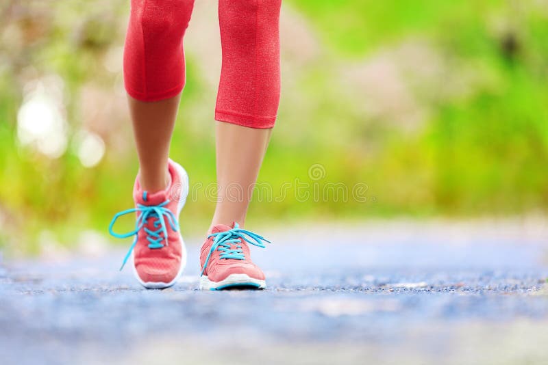 Jogging woman with athletic legs and running shoes. Female walking on trail in forest in healthy lifestyle concept with close up on running shoes. Female athlete jogger training outdoors.