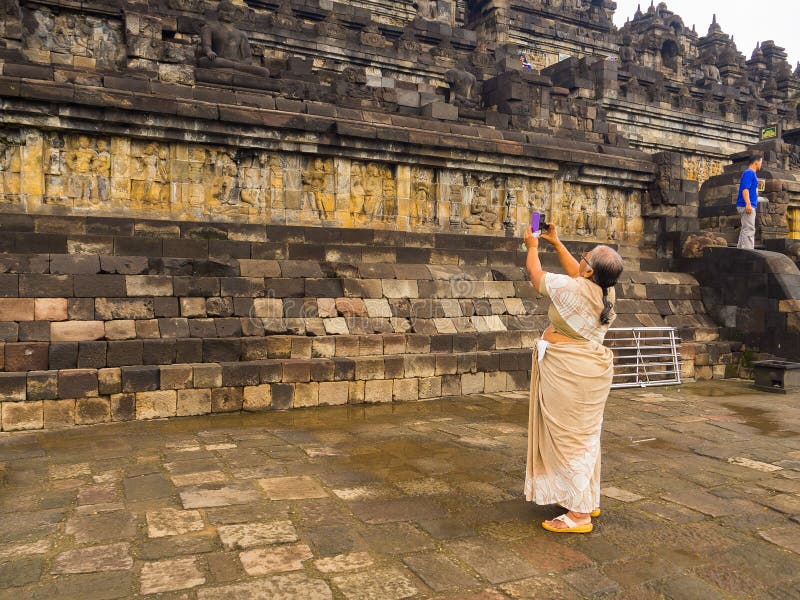 JOGJA, INDONÉSIE - 12 août, 2O17 : Femme non identifiée prenant des photos d'un mur avec le soulagement de Bas, temple de Borobud photographie stock JOGJA, INDONÉSIE - 12 août, 2O17 : Femme non identifiée prenant des photos d'un mur avec le soulagement de Bas, temple de Borobud photographie stock