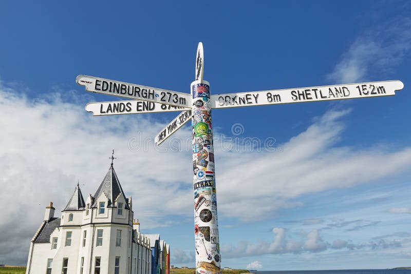 Britains lands end sign at john o`groats in scotland with blue skies and ocean and grass in background. Has many stickers on post