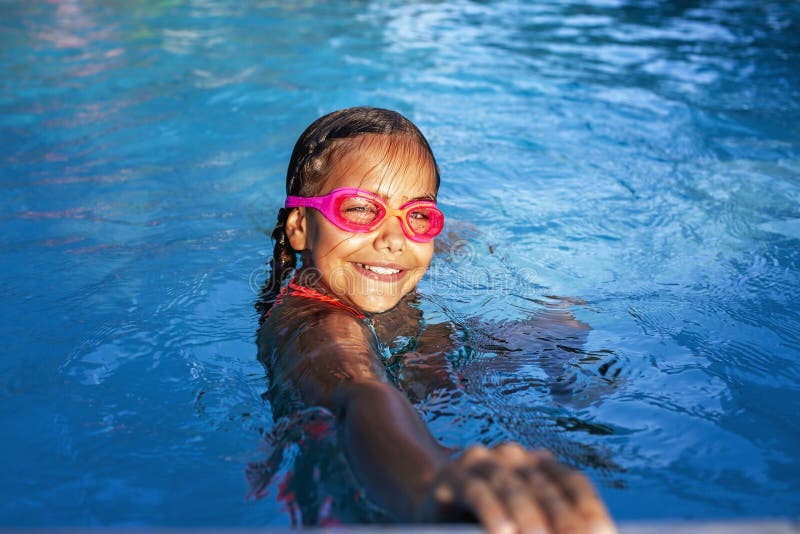 Joie vive dans la piscine : un enfant aux lunettes roses sourit dans l'eau. image libre de droits