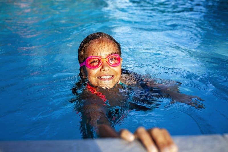 Joie vive dans la piscine : un enfant aux lunettes roses sourit dans l'eau. photographie stock