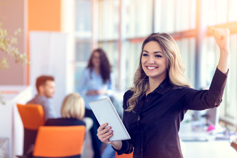 Join a digital age. Cheerful young woman holding digital tablet while his friends working on background stock photo Join a digital age. Cheerful young woman holding digital tablet while his friends working on background stock photo
