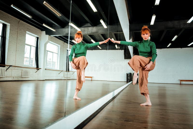 Joli danseur professionnel roux dans un col roulé vert faisant la gymnastique rythmique photographie stock Joli danseur professionnel roux dans un col roulé vert faisant la gymnastique rythmique photographie stock
