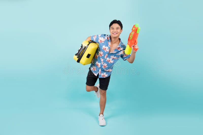 Joli homme de tourisme asiatique en tenue d'été avec pistolet à eau et valise en bleu studio isolé photographie stock libre de droits