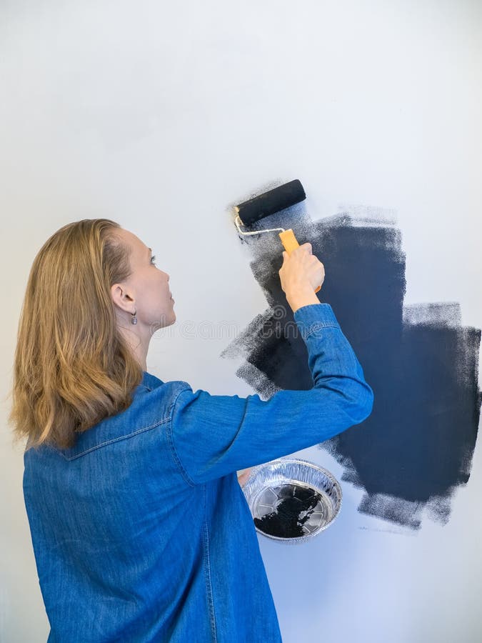 Jolie femme avec un rouleau peint le mur noir. concept de réparation. espace de copie. vue verticale photographie stock