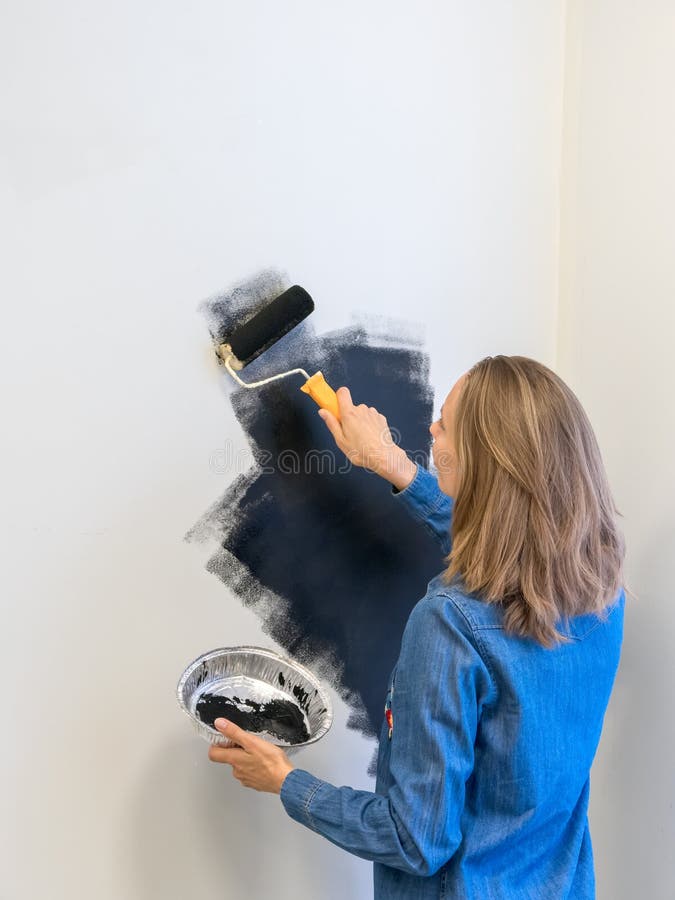 Jolie femme avec un rouleau peint le mur noir. concept de réparation. espace de copie. vue verticale images stock