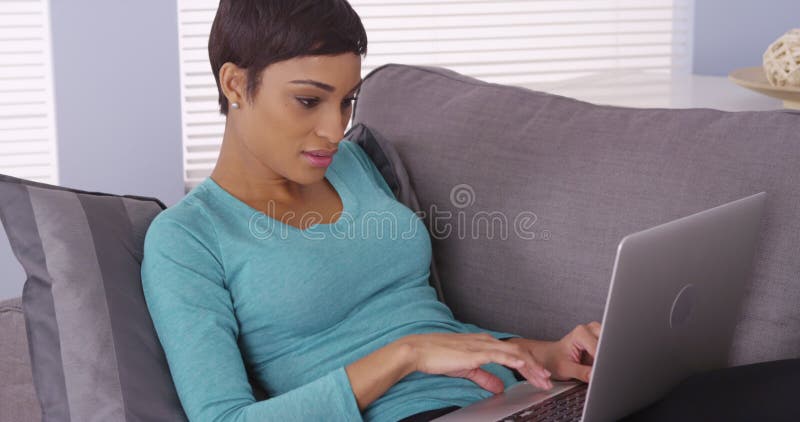 Jolie femme noire utilisant un ordinateur portable sur le canapé
