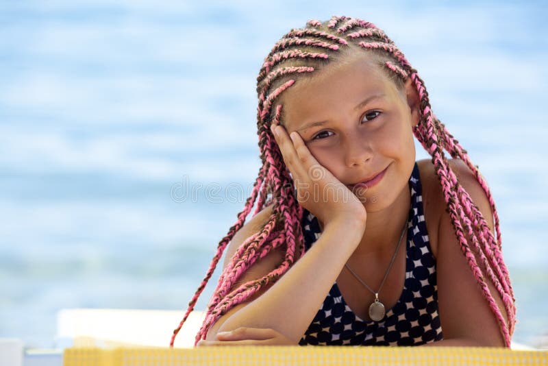 Jolie fille avec les dreadlocks africains roses se trouvant sur le canap? jaune du soleil, regardant la cam? ra avec le sourire, l images stock