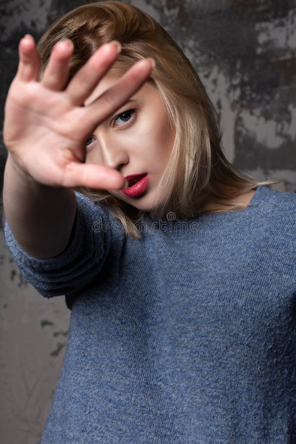 Jolie fille à la mode utilisant le chandail bleu, étirant sa main dans la caméra et couvrant son visage images libres de droits Jolie fille à la mode utilisant le chandail bleu, étirant sa main dans la caméra et couvrant son visage images libres de droits