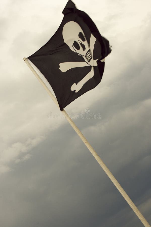 A Jolly Roger Pirate flag in black and white with skull in crossbones flies high in the sky. A Jolly Roger Pirate flag in black and white with skull in crossbones flies high in the sky.