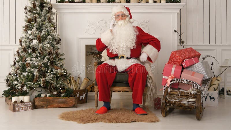 Jolly Santa Claus sammanträde vid julgranen och samtal på telefonen arkivbild Jolly Santa Claus sammanträde vid julgranen och samtal på telefonen arkivbild