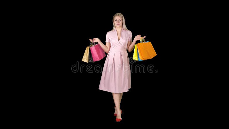 Jong blondemeisje in roze kleding die aan camera het winkelen zakken tonen en het lopen, Alpha Channel