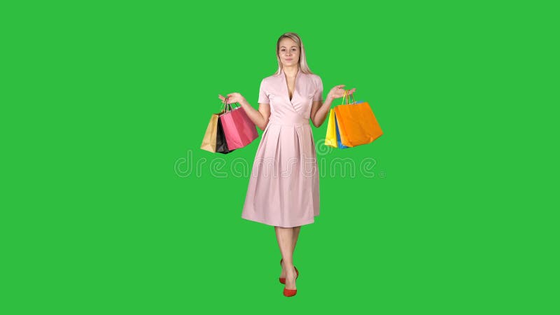 Jong blondemeisje in roze kleding die aan camera het winkelen zakken tonen en het lopen op het Groen Scherm, Chromasleutel