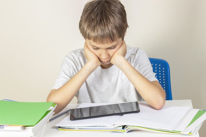 Jong geitjezitting bij lijst met boeken notitieboekjes en het gebruiken van tabletcomputer stock foto Jong geitjezitting bij lijst met boeken notitieboekjes en het gebruiken van tabletcomputer stock foto