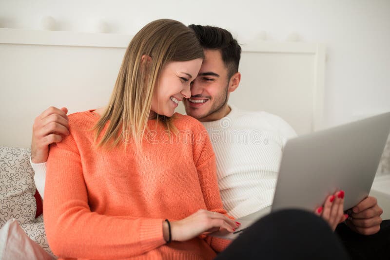 Jong gelukkig paar die laptop op bed met behulp van stock fotografie Jong gelukkig paar die laptop op bed met behulp van stock fotografie