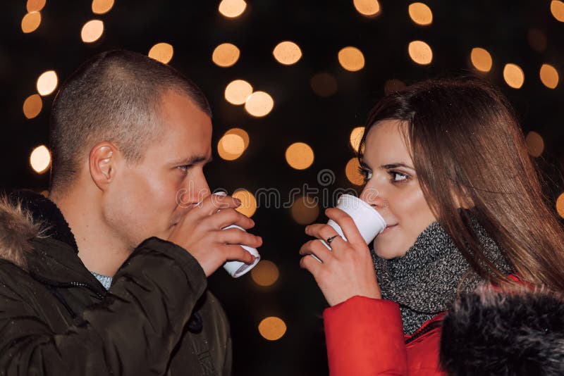 Close up side profile photo of beautiful young couple outdoors on a winter eve, with hot drinks, looking at each other, so tender, romantic, tempting, sensual. True love and feelings - Image. Close up side profile photo of beautiful young couple outdoors on a winter eve, with hot drinks, looking at each other, so tender, romantic, tempting, sensual. True love and feelings - Image