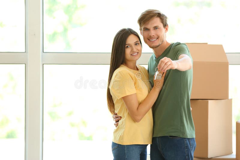 Jong gelukkig paar met sleutel van hun nieuw huis en bewegende dozen binnen stock afbeelding Jong gelukkig paar met sleutel van hun nieuw huis en bewegende dozen binnen stock afbeelding