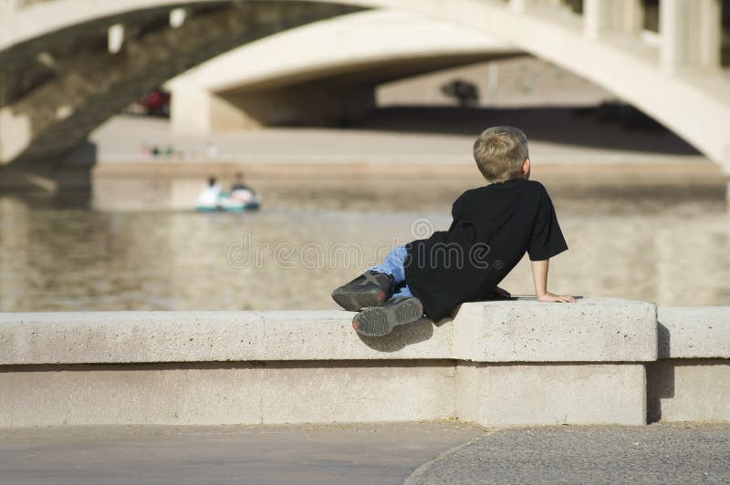 A young child observes others boating on an inner city waterway. A young child observes others boating on an inner city waterway.