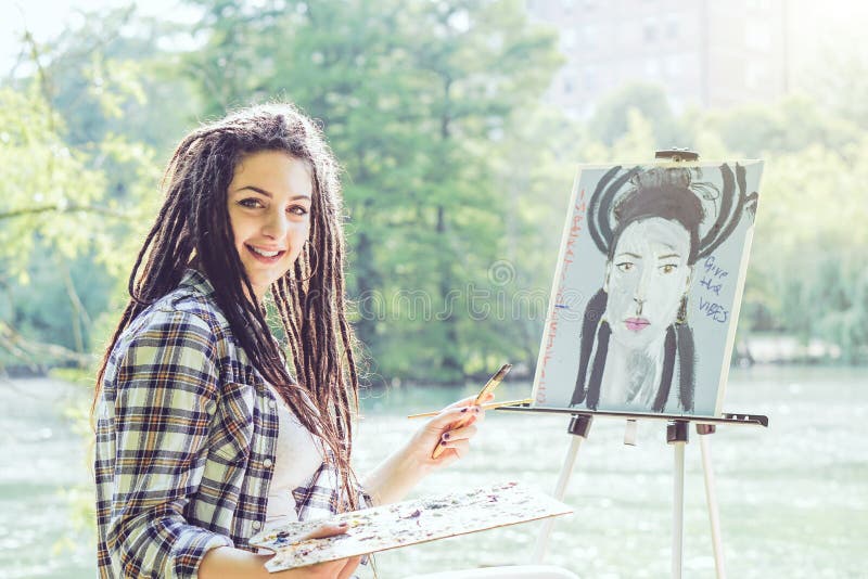 Jong kunstenaarsmeisje die een zelfportret in een park schilderen dichtbij meer - Schildersvrouw met dreadlockskapsel die aan haa stock foto's Jong kunstenaarsmeisje die een zelfportret in een park schilderen dichtbij meer - Schildersvrouw met dreadlockskapsel die aan haa stock foto's