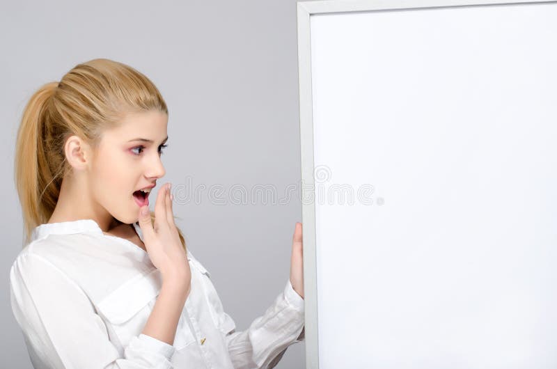 Jong meisje die verraste status dichtbij een witte raad kijken. stock foto's Jong meisje die verraste status dichtbij een witte raad kijken. stock foto's