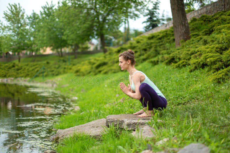 Jong mooi Kaukasisch donkerbruin meisje die yoga op een groen gazon doen tegen de achtergrond van de rivier royalty-vrije stock foto's Jong mooi Kaukasisch donkerbruin meisje die yoga op een groen gazon doen tegen de achtergrond van de rivier royalty-vrije stock foto's