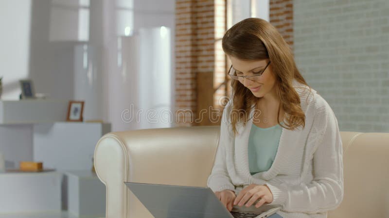 Jong mooi meisje die in glazen op laptop, glimlach bij camera babbelen