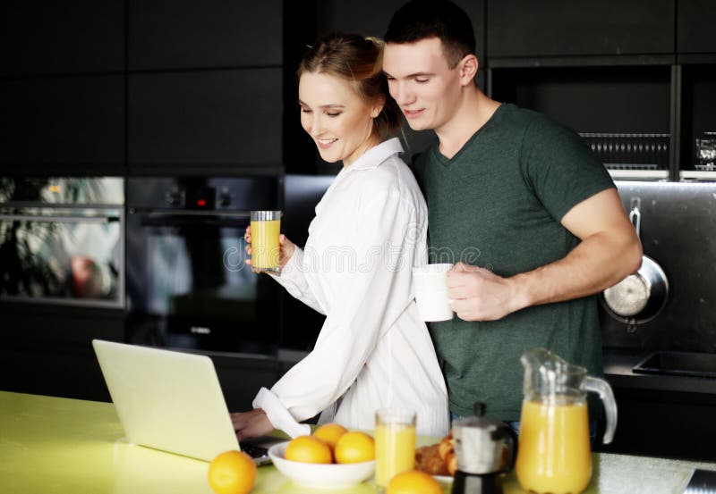 Jong paar die thuis koffie in keuken hebben en aan laptop computer werken stock afbeeldingen Jong paar die thuis koffie in keuken hebben en aan laptop computer werken stock afbeeldingen