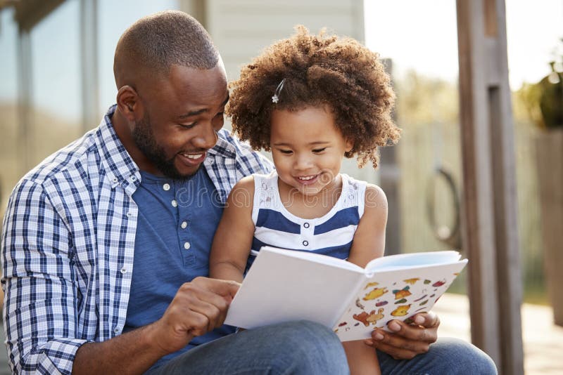 Young black father and daughter reading book outside. Young black father and daughter reading book outside