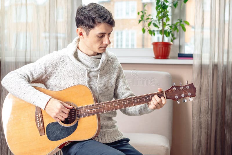 Jonge aantrekkelijke mannelijke musicuszitting op een stoel die akoestische gitaar in ruimte spelen Concept muziek als hobby stock foto's Jonge aantrekkelijke mannelijke musicuszitting op een stoel die akoestische gitaar in ruimte spelen Concept muziek als hobby stock foto's