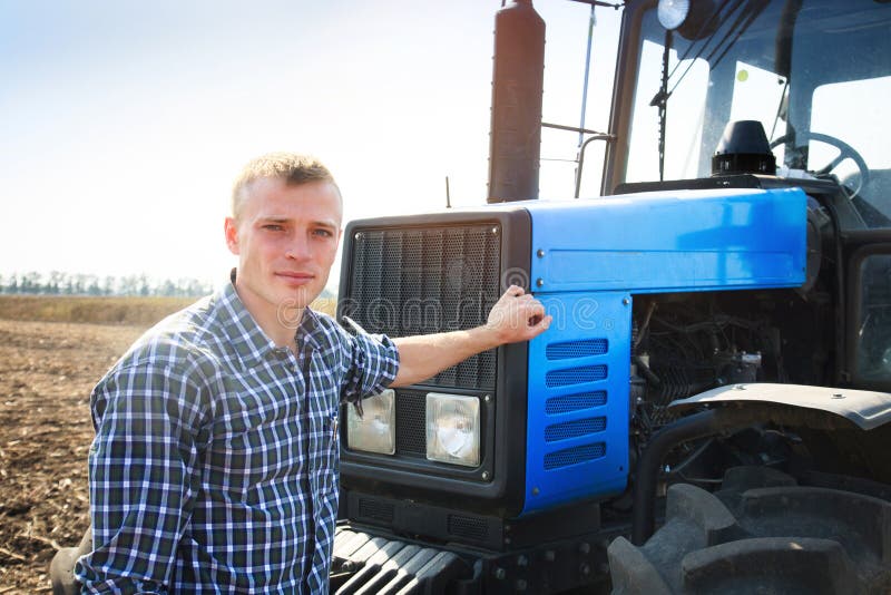 Jonge aantrekkelijke mens dichtbij een tractor Concept landbouw royalty-vrije stock afbeeldingen Jonge aantrekkelijke mens dichtbij een tractor Concept landbouw royalty-vrije stock afbeeldingen