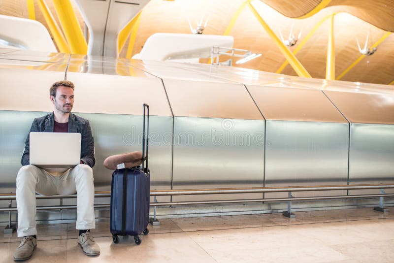Jonge aantrekkelijke mensenzitting bij de luchthaven die met een lapto werken stock foto Jonge aantrekkelijke mensenzitting bij de luchthaven die met een lapto werken stock foto