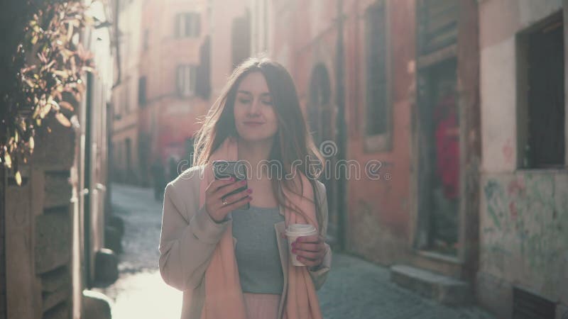 Jonge aantrekkelijke vrouw die in stad lopen en smartphone gebruiken Meisje die met vrienden en het drinken koffie babbelen stock fotografie Jonge aantrekkelijke vrouw die in stad lopen en smartphone gebruiken Meisje die met vrienden en het drinken koffie babbelen stock fotografie