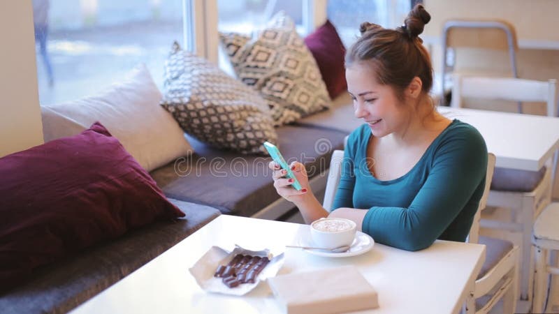 Jonge, aantrekkelijke vrouwenzitting bij koffie die mobiele telefoon en het lachen gebruiken stock videobeelden Jonge, aantrekkelijke vrouwenzitting bij koffie die mobiele telefoon en het lachen gebruiken stock videobeelden