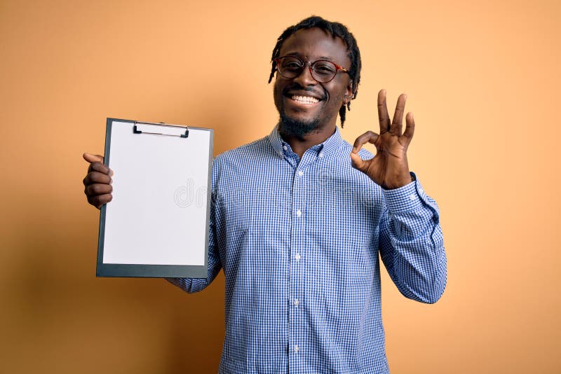 Young african american inspector man wearing glasses holding clipboard checklist doing ok sign with fingers, excellent symbol. Young african american inspector man wearing glasses holding clipboard checklist doing ok sign with fingers, excellent symbol