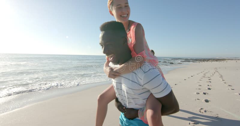 Jonge afrikaanse amerikaanse man geeft een gyback lift naar een jonge kaukasische vrouw op het strand