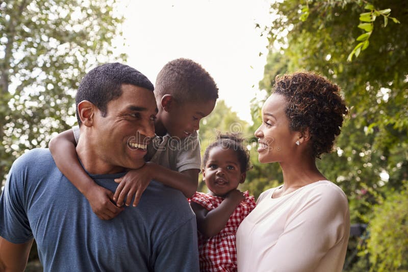 Jonge Afrikaanse Amerikaanse ouders die kinderen in tuin vervoeren stock foto's Jonge Afrikaanse Amerikaanse ouders die kinderen in tuin vervoeren stock foto's