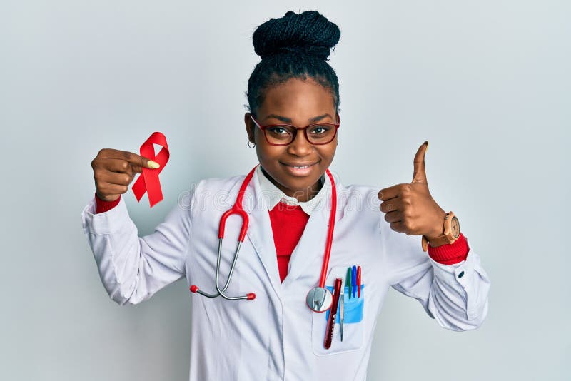 Young african american woman wearing doctor uniform holding support red ribbon smiling happy and positive, thumb up doing excellent and approval sign. Young african american woman wearing doctor uniform holding support red ribbon smiling happy and positive, thumb up doing excellent and approval sign