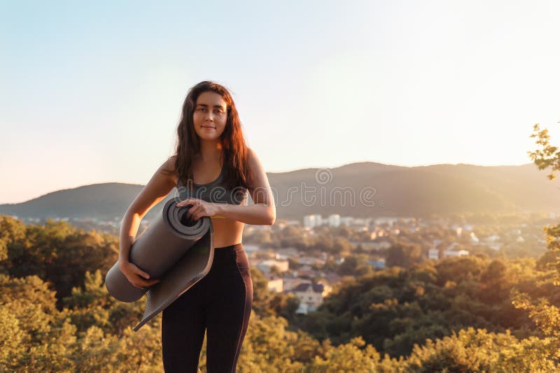 Jonge atletische vrouw die een yogamat houden Het concept sport, fitness en gezonde levensstijl Zonsondergang en dorp dichtbij be royalty-vrije stock foto's Jonge atletische vrouw die een yogamat houden Het concept sport, fitness en gezonde levensstijl Zonsondergang en dorp dichtbij be royalty-vrije stock foto's