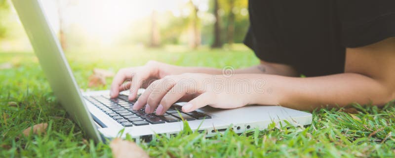 Jonge Aziatische vrouwen` s benen op het groene gras met open laptop Meisjes` s handen op toetsenbord Het Concept van het Afstand