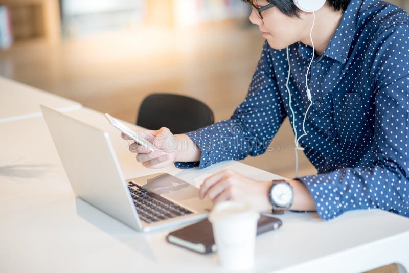 Jonge Aziatische zakenman die smartphone gebruiken die met laptop werken stock foto Jonge Aziatische zakenman die smartphone gebruiken die met laptop werken stock foto
