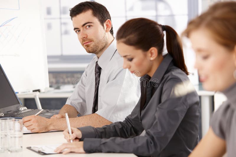 Young office workers having business training, sitting at meeting table, writing notes. Young office workers having business training, sitting at meeting table, writing notes.