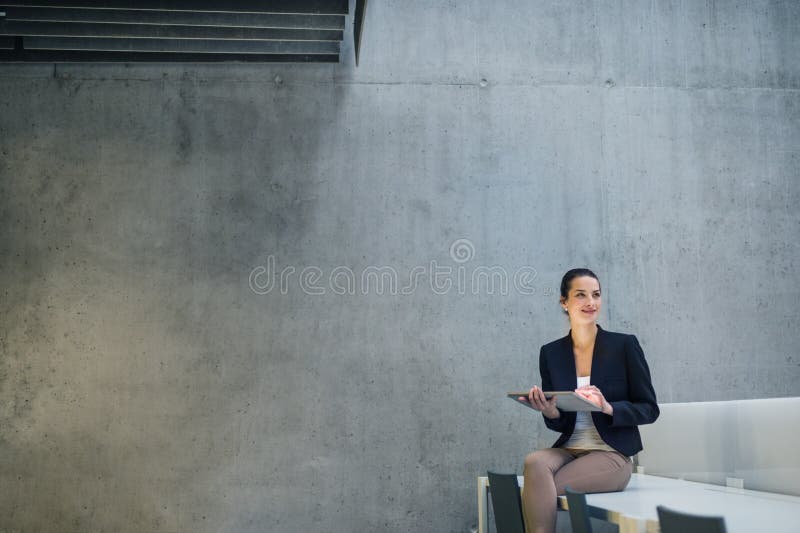 Jonge bedrijfsvrouw met tabletzitting op bureau tegen concrete muur in bureau royalty-vrije stock afbeeldingen Jonge bedrijfsvrouw met tabletzitting op bureau tegen concrete muur in bureau royalty-vrije stock afbeeldingen