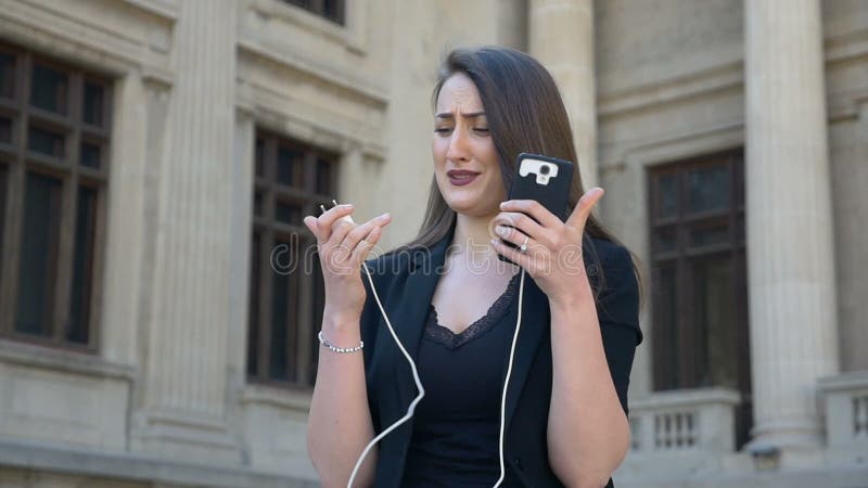Jonge boze en bezorgde vrouw die terwijl haar telefoondraaien weg wegens geloste lage batterij in de stad schreeuwen