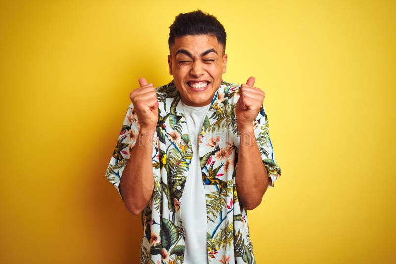 Young brazilian man on vacation wearing summer floral shirt over isolated yellow background excited for success with arms raised and eyes closed celebrating victory smiling. Winner concept. Young brazilian man on vacation wearing summer floral shirt over isolated yellow background excited for success with arms raised and eyes closed celebrating victory smiling. Winner concept