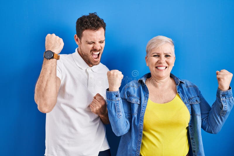 Young brazilian mother and son standing over blue background celebrating surprised and amazed for success with arms raised and eyes closed. winner concept. Young brazilian mother and son standing over blue background celebrating surprised and amazed for success with arms raised and eyes closed. winner concept