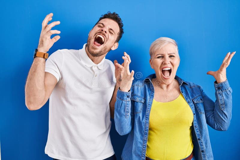 Young brazilian mother and son standing over blue background celebrating mad and crazy for success with arms raised and closed eyes screaming excited. winner concept. Young brazilian mother and son standing over blue background celebrating mad and crazy for success with arms raised and closed eyes screaming excited. winner concept