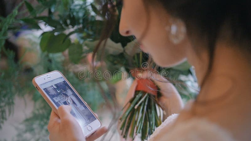 Jonge bruid op huwelijksdag die mobiele telefoon met behulp van